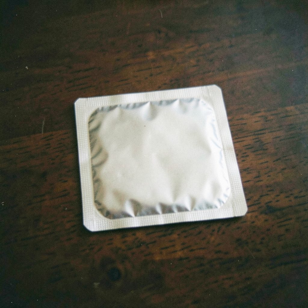 A grainy analog photograph of a single blister pack with silver foil backing, resting on a dark walnut tabletop, subdued tones.